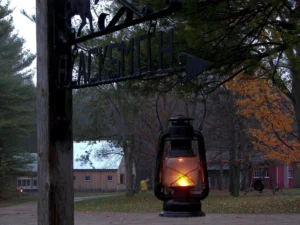 A glowing lantern hangs on sign with the word 'blacksmith'. It is dusk and historical buildings are in the background.